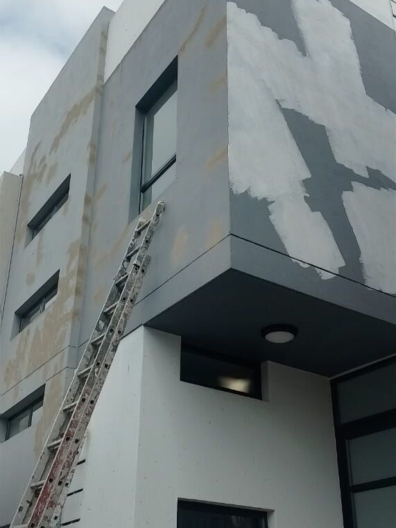 Double-storey exterior during preparation: cracks filled and patches primed, with a ladder against the wall